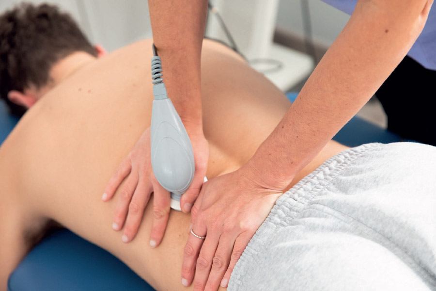 Una persona si sottopone a un massaggio di fisioterapia con un apparecchio portatile per alleviare la tensione muscolare.